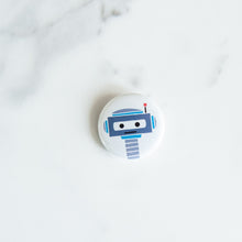 Load image into Gallery viewer, A button pin on a white tabletop. The button features an illustration of a blue and grey robot.