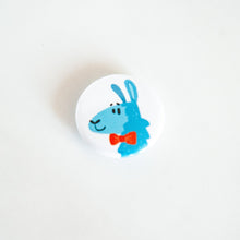 Load image into Gallery viewer, A buttons on a white tabletop. The button features a blue illustrated llama with a red bow tie. 