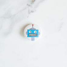 Load image into Gallery viewer, A button pin on a white tabletop. The button features an illustration of a blue robot.