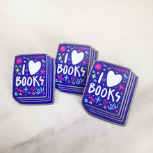 Load image into Gallery viewer, Three enamel pins with the words &#39;I love books&quot; with the word love shown as a heart. The words are featured inside an illustrated book, all in bright fun colors. 