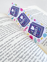 Load image into Gallery viewer, A bookmark placed inside a book. The bookmark features the words &quot;i love books&quot; with love shown shaped as a heart. The words are placed inside an illustrated book. 