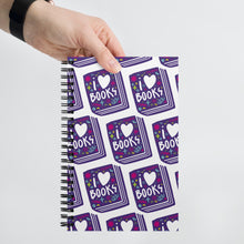 Load image into Gallery viewer, A spiral notebook being held by a person. The white spiral notebook has black spiral binding. The pattern design features the words &quot;I love books&quot; inside an illustrated book with the word love as a heart. 