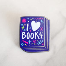 Load image into Gallery viewer, An enamel pin with the words &#39;I love books&quot; with the word love shown as a heart. The words are featured inside an illustrated book, all in bright fun colors. 