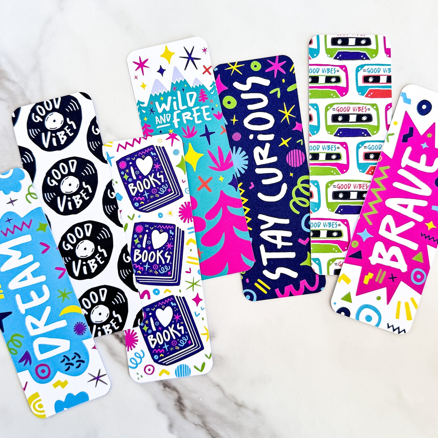 A image of seven bookmarks featuring illustrated word designs with the words dream, good vibes, i love books, wild and free, stay curious, and brave. 