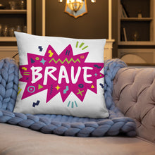 Load image into Gallery viewer, A white pillow on a sofa with a blue knitted blanket. The white pillow features the artwork on a white background with a hot pink star with the word &#39;brave&#39; inside and sketchy, fun elements around the word. 