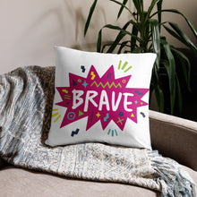 Load image into Gallery viewer, A pillow on a sofa with a blanket. The white pillow features the artwork on a white background with a hot pink star with the word &#39;brave&#39; inside and sketchy, fun elements around the word. 