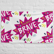 Load image into Gallery viewer, A large flag featured on a white brick wall. The white flag features a pattern with the word &quot;brave&quot; featured inside a pink star-like shape with sketchy illustrations around the word. 