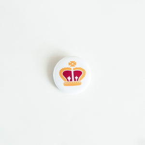 A button on white tabletop. The button features an illustration of a royal crown. 