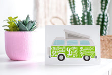 Load image into Gallery viewer, A greeting card featured standing up on a white tabletop with a pink plant pot in the background and some succulents in the pot. There’s a woven basket in the background with a cactus inside. The card features the words “Difficult roads often lead to beautiful destinations” with an illustrated campervan.