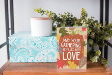 Load image into Gallery viewer, A greeting card is on a table top with a present in the background. There&#39;s greenery on top of the present. The card reads &quot;May Your Gathering Be Filled with Love&quot; with the words inside an illustrated pumpkin with leaves surrounding the pumpkin.