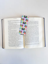 Load image into Gallery viewer, A bookmark placed inside a book. The bookmark features the words &quot;good vibes&quot; inside an illustrated cassette tape. 