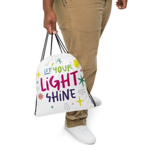 Load image into Gallery viewer, A person holding a white drawstring bag. The drawstring bag has the words &quot;Let Your Light Shine&quot; with sketchy illustrations around the words.