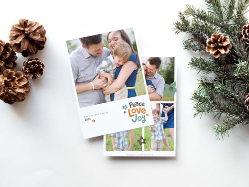 A photo of a double-sided Christmas card showing the front and back of the card laying on a white surface. Around the two sides of the card are pine cones and pine needles. The front of the card features a photo with the words “Peace Love joy” to the bottom right and space to the bottom left to put your family names. The words feature some modern illustrated flowers around it. The back of the card features three photos with modern illustrated flowers.