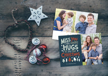 Load image into Gallery viewer, A photo of a Christmas card showing the front and back of the card laying on a wood surface. To the left of the cards are some ornaments. The front of the card features a photo on the right side and on the left side are the words “ Miss you and sending hugs to you this Christmas” with illustrated trees below the words. The back of the card features two photos with illustrated trees at the bottom.