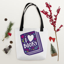 Load image into Gallery viewer, A white tote bag with black handles on a wood tabletop with Christmas items around it. The tote bag has a design with the words &#39;I love books&#39; with the word love shown as a heart. The words are inside an illustrated book. 