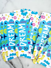 Load image into Gallery viewer, A group of bookmarks on a tabletop. The bookmark design has the word &quot;dream&quot; inside a teal cloud-like shape with sketchy, whimsical items around. 