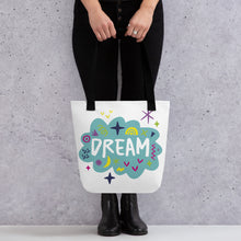 Load image into Gallery viewer, A person holding a white tote bag with black handles. The bag features a design with the word &#39;dream&#39; with an illustrated cloud around the word with colorful sketchy around. 