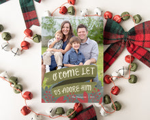 Load image into Gallery viewer, A photo of a one-sided Christmas card showing the front of the card laying on white table top. The card is surrounded by plaid red and green ribbon and red, green and white bells. The photo card features one photo with the words “O Come Let Us Adore Him” below with illustrated red leaves.  