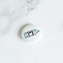 Load image into Gallery viewer, A button pin on a white tabletop. The button features an illustration of a crayon. 