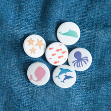 Load image into Gallery viewer, A set of six buttons on a jean jacket. The buttons feature illustrations of whales, fish, starish, dolphins, and an octopus. 