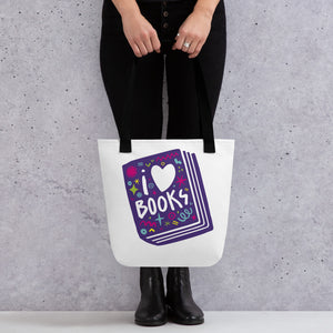 A person holding a white tote bag with black handles. The tote bag has a design with the words 'I love books' with the word love shown as a heart. The words are inside an illustrated book. 