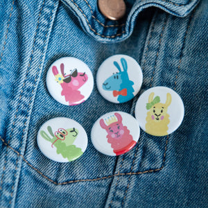 A set of five buttons on a jean jacket. The buttons feature five different colorful, illustrated llamas. 