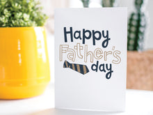 Load image into Gallery viewer, A greeting card is on a table top with a yellow plant pot and a green plant inside. The card features the words “Happy Father’s  Day” with a striped tie on the bottom of the words. 