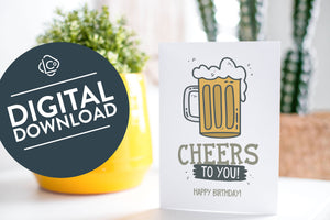 A greeting card is on a table top with a yellow plant pot and a green plant inside. The card features the words “Cheers to You! Happy Birthday!” with an illustrated beer mug. The words "digital download" are featured in a circle on top of the image.