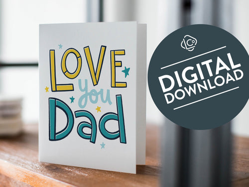 A card on a wood tabletop with an object in the background that is out of focus. The card features the words “Love you Dad” with small stars around the letters. The words 