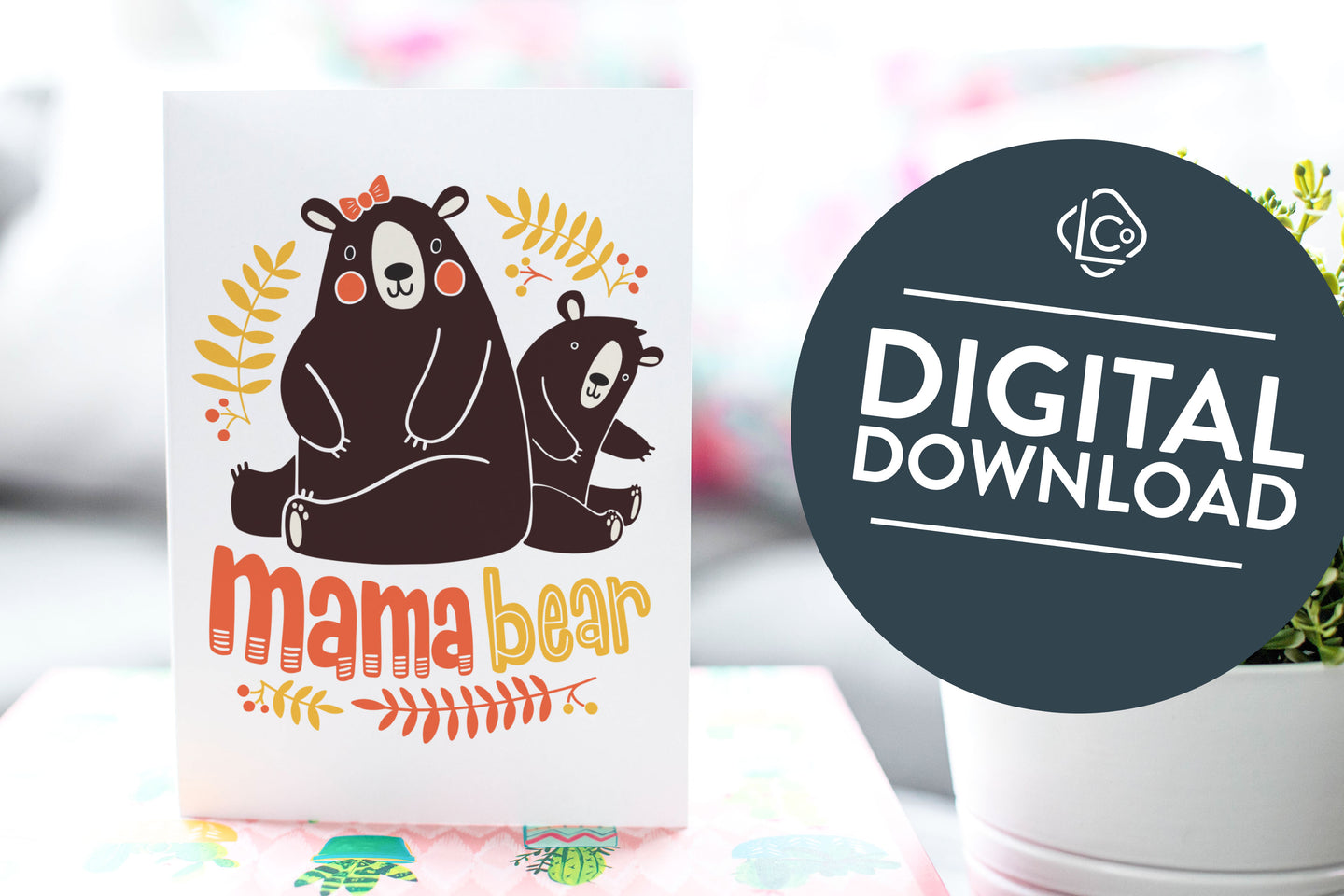 A greeting card is on a table top with a gift in pink wrapping paper. Next to the gift is a white plant pot with a green plant. The card features the words “Mama Bear” with an illustrated mama bear and baby bear. The words 