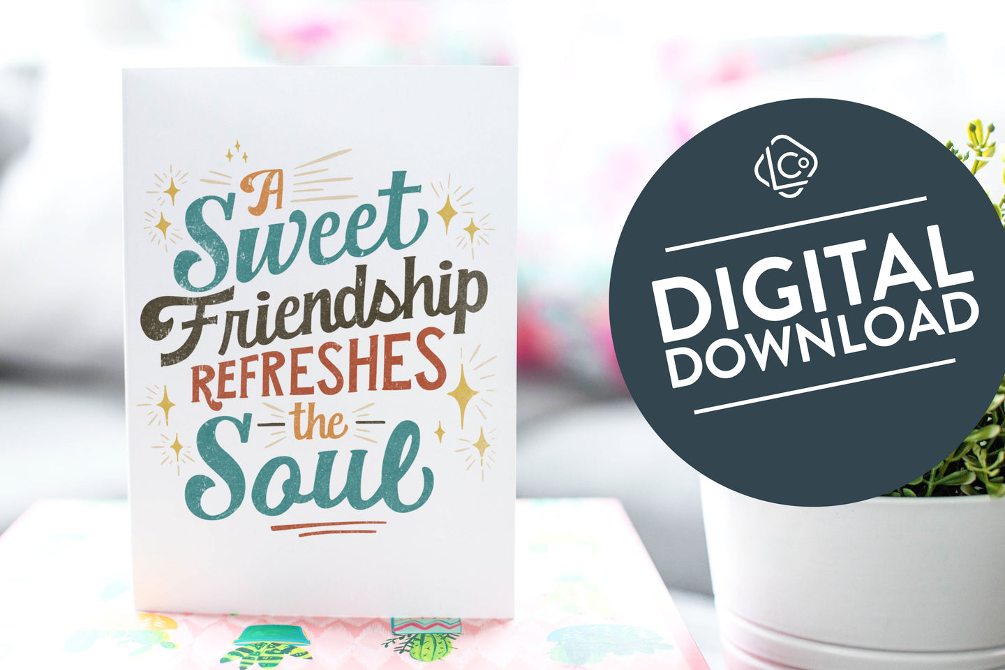A greeting card is on a table top with a gift in pink wrapping paper. Next to the gift is a white plant pot with a green plant. The card features the words “A sweet friendship refreshes the soul.”  The words 