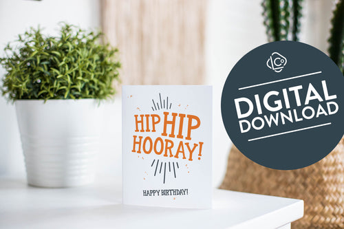 A greeting card is featured on a white tabletop with a white planter in the background with a green plant. There’s a woven basket in the background with a cactus inside. The card features the words “Hip Hip Hooray! Happy Birthday!” The words 