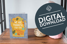 Load image into Gallery viewer, A greeting card featured standing up on a white tabletop with a pink plant pot with succulents, a pink rock and a small woven basket. The card features the words &quot;We are Thankful for You&quot; with the words featured inside an illustrated teapot. The words &quot;digital download&quot; are featured in a circle over the image.