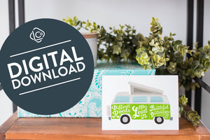 A greeting card is on a table top with a present in blue wrapping paper in the background. On top of the present is a candle and some greenery from a plant too. The card features the words “Difficult roads often lead to beautiful destinations” with an illustrated campervan. The words "digital download" are featured in a circle on top of the image. 