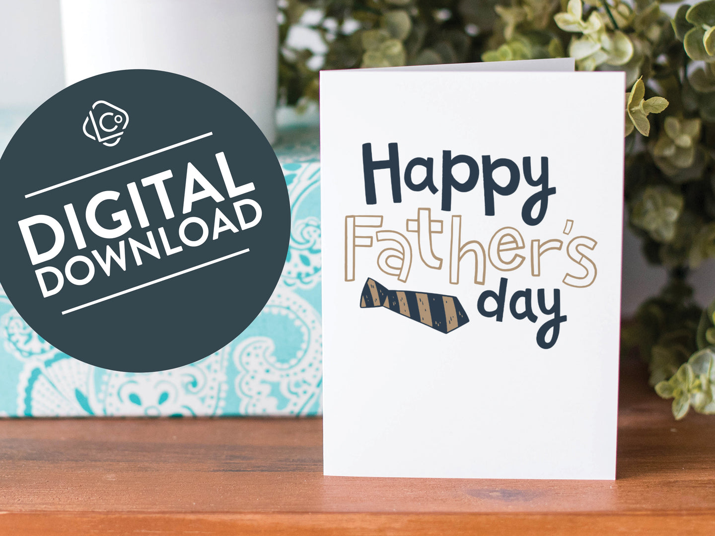 A greeting card is on a table top with a present in blue wrapping paper in the background. On top of the present is a candle and some greenery from a plant too. The card features the words  “Happy Father’s  Day” with a striped tie on the bottom of the words. The words 