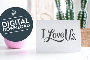 A greeting card featured standing up on a white tabletop with a pink plant pot in the background and some succulents in the pot. There’s a woven basket in the background with a cactus inside. The card features the words “I Love Us.” The words "digital download" are featured in a circle on top of the image. 
