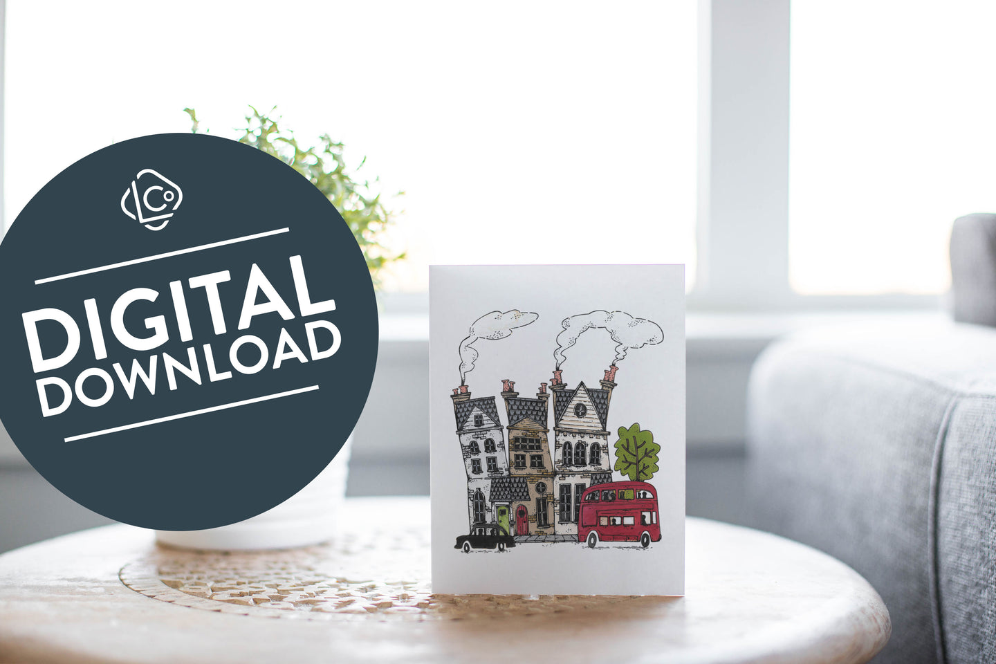 A greeting card laying on a wooden table with some cut wood details. The card features the a design with illustrated London houses, a black taxi cab and a red double decker bus. The words 