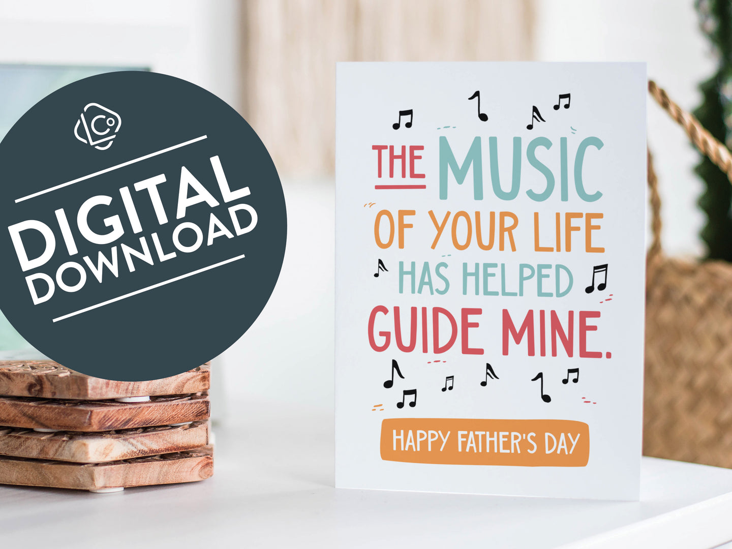 A greeting card featured standing up on a white tabletop with a framed photo of a succulent in the background and a stack of wooden coasters. There’s a woven basket in the background with a cactus inside. The card features the words “The music of your life has helped guide mine. Happy Father's Day.” The words 