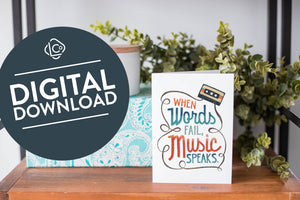 A greeting card is on a table top with a present in blue wrapping paper in the background. On top of the present is a candle and some greenery from a plant too. The card features the words “When words fail, music speaks.” The words "digital download" are featured in a circle on top of the image. 