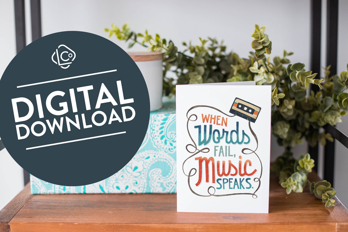 A greeting card is on a table top with a present in blue wrapping paper in the background. On top of the present is a candle and some greenery from a plant too. The card features the words “When words fail, music speaks.” The words 
