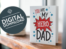 Load image into Gallery viewer, A card on a wood tabletop with an object in the background that is out of focus. The card features the words &quot;You are my hero Dad.” The words &quot;digital download&quot; are featured in a circle on top of the image.