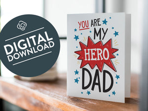 A card on a wood tabletop with an object in the background that is out of focus. The card features the words "You are my hero Dad.” The words "digital download" are featured in a circle on top of the image.