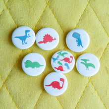 Load image into Gallery viewer, A set of seven buttons on a yellow background. The buttons feature illustrations of a Pterodactyl, Sauropod, Stegosaurus, T-Rex, Triceratops, Velociraptor, and a button with all on one button. 