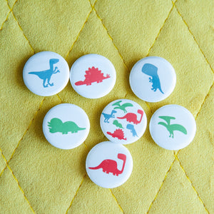 A set of seven buttons on a yellow background. The buttons feature illustrations of a Pterodactyl, Sauropod, Stegosaurus, T-Rex, Triceratops, Velociraptor, and a button with all on one button. 