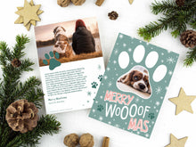 Load image into Gallery viewer, A photo of a two-sided Christmas card showing the front of the card on top of a brown wrapped gift on a white tabletop. Around the gift are pine needles, pinecones and wood star ornaments. The front of the card features a photo inside a paw shaped frame. Around the photo are white stars and below are the words “Merry Woofmas.” The back of the card features one photo with a dog paw illustration and space to add an update.