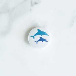 A button on a white tabletop. The button features an illustration of dolphins. 