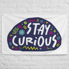 Load image into Gallery viewer, A large flag featured on a white brick wall. The white flag features the words &quot;stay curious&quot; featured inside a a purple shape with sketchy illustrations around. 