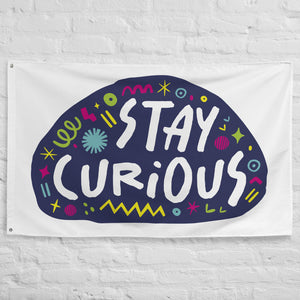 A large flag featured on a white brick wall. The white flag features the words "stay curious" featured inside a a purple shape with sketchy illustrations around. 