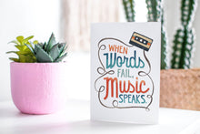 Load image into Gallery viewer, A greeting card featured standing up on a white tabletop with a pink plant pot in the background and some succulents in the pot. There’s a woven basket in the background with a cactus inside. The card features the words “When words fail, music speaks.”