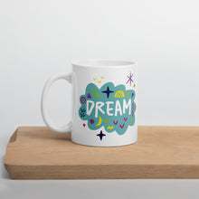 Load image into Gallery viewer, A white mug on a wood board. The mug features a design with the word &#39;dream&#39; in an illustrated cloud with sketchy elements around it. 